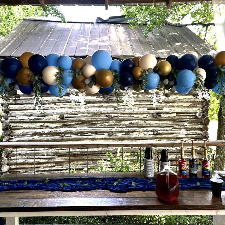 Navy, blue and gold over-the-table balloon garland with greenery above a drink station in Wake Forest, NC