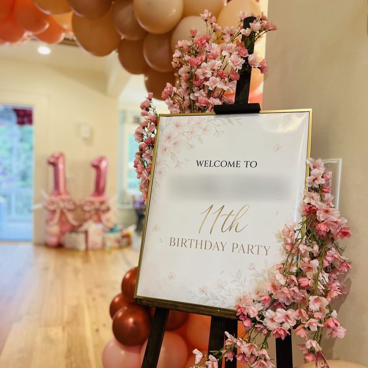 Custom welcome sign on an easel framed by cherry blossoms and blush balloons