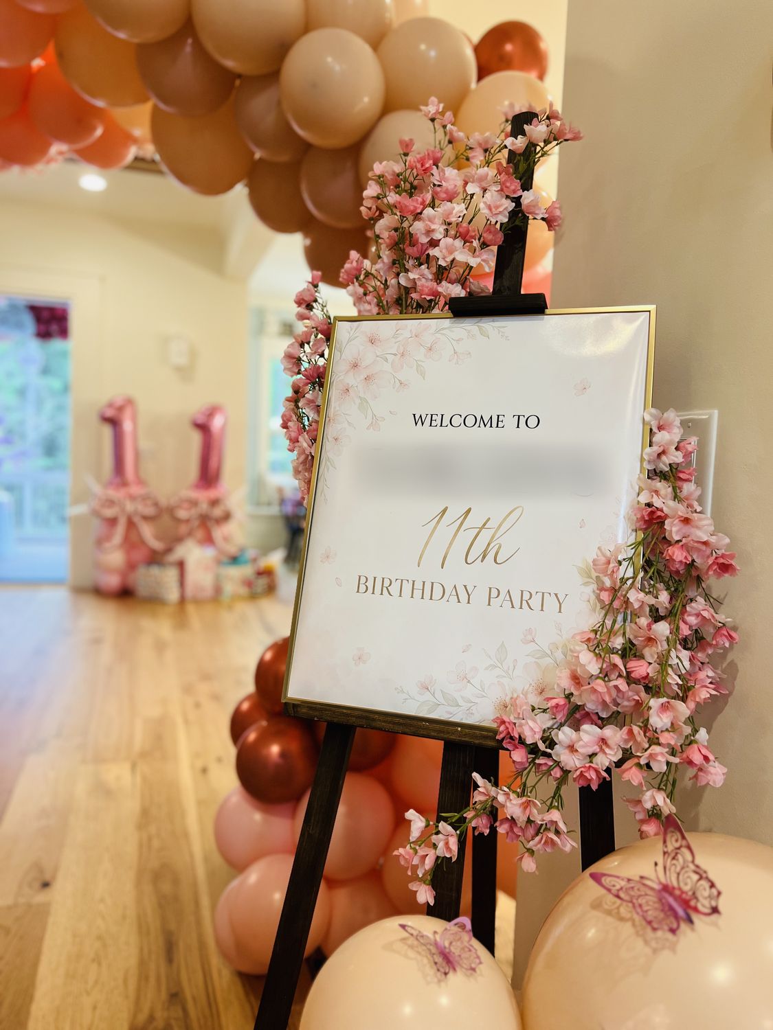 Custom welcome sign on an easel framed by cherry blossoms and blush balloons